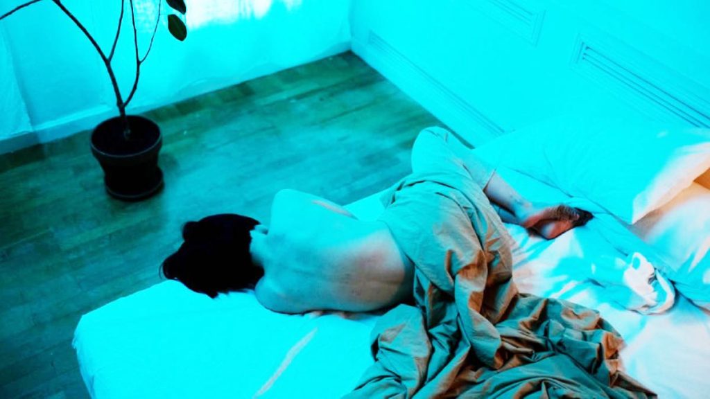 Femme allongée dans une ambiance apaisante, explorant son corps avec douceur et bienveillance.