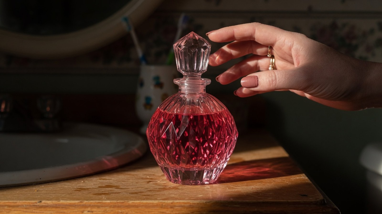 Bouteille de parfum rose facettée sur vanité en bois, reflets de lumière rose