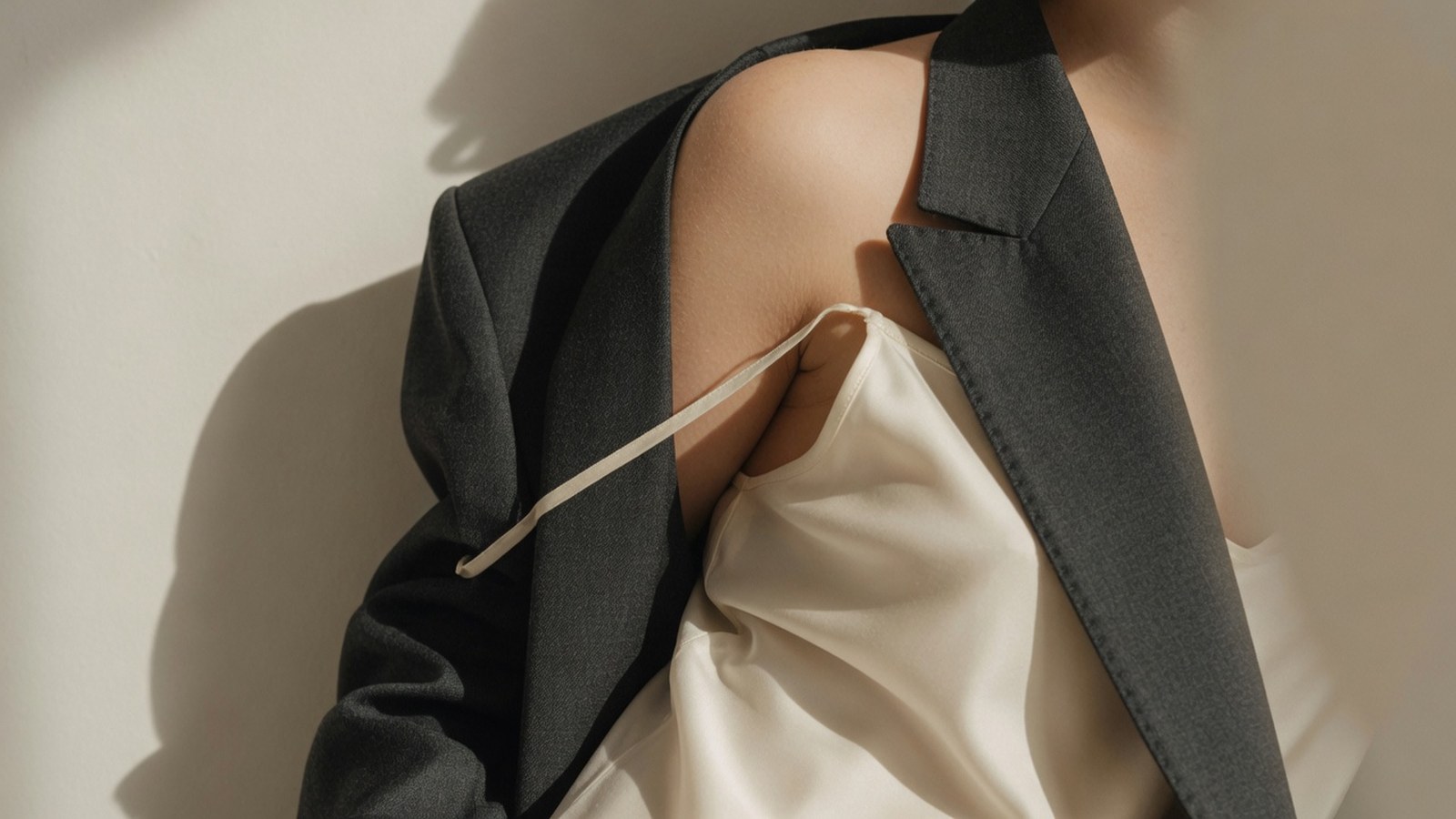 Femme sans visage portant robe soie crème et blazer laine taupe, détail épaule éditorial mode.