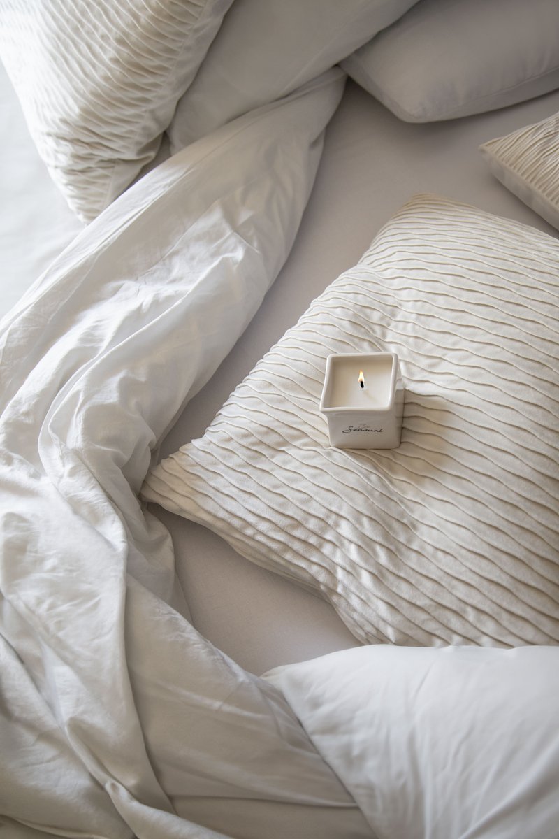 Bougie de massage Be Sensual allumee sur du linge de lit