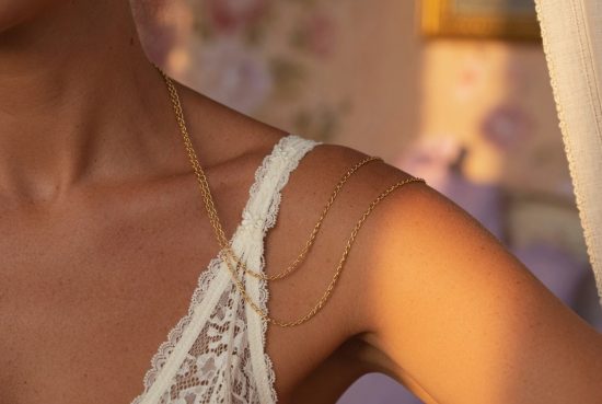 Détail de la clavicule et de l'épaule d'une femme en soutien-gorge en dentelle ivoire avec chaîne dorée fine, sur peau bronzé