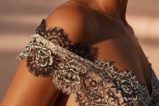 Femme en profil, épaule nue bronzée, dentelle écru drapiée sur la peau créant des motifs d'ombre.