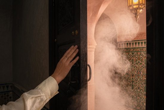 Main poussant une porte en bois massif d'un hammam parisien, vapeur chaude et lumière dorée s'échappant, carrelage zellige vi