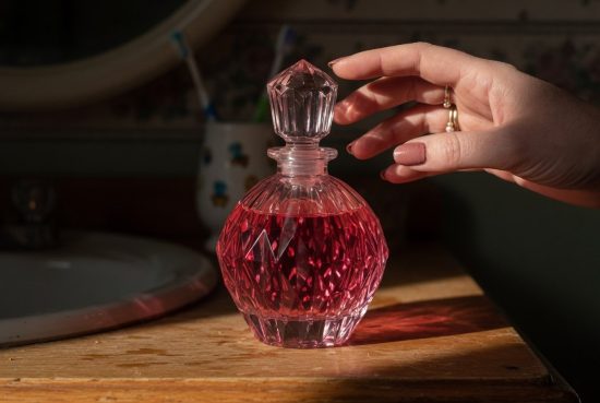 Bouteille de parfum rose facettée sur vanité en bois, reflets de lumière rose