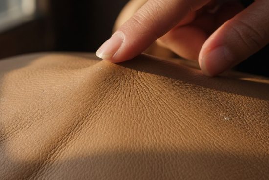 Doigt appuyant sur du cuir camel, indentation visible du doigt dans le matériau