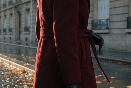 Femme vue de dos portant un long manteau bordeaux sur une rue pavée parisienne à la lumière dorée du soir.