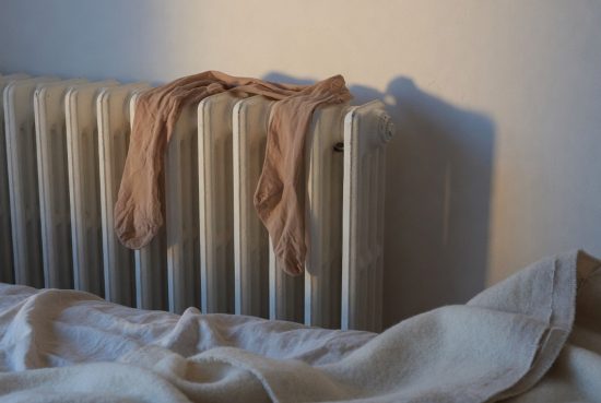 hero-8 Radiateur blanc en fonte dans une chambre, mur crème, lumière latérale douce, tissu drapé.