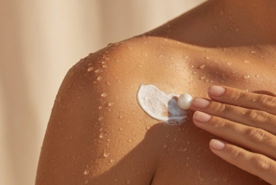 Épaule bronzée et humide après la douche, une main applique délicatement une noisette de crème après-soleil sur la peau dorée